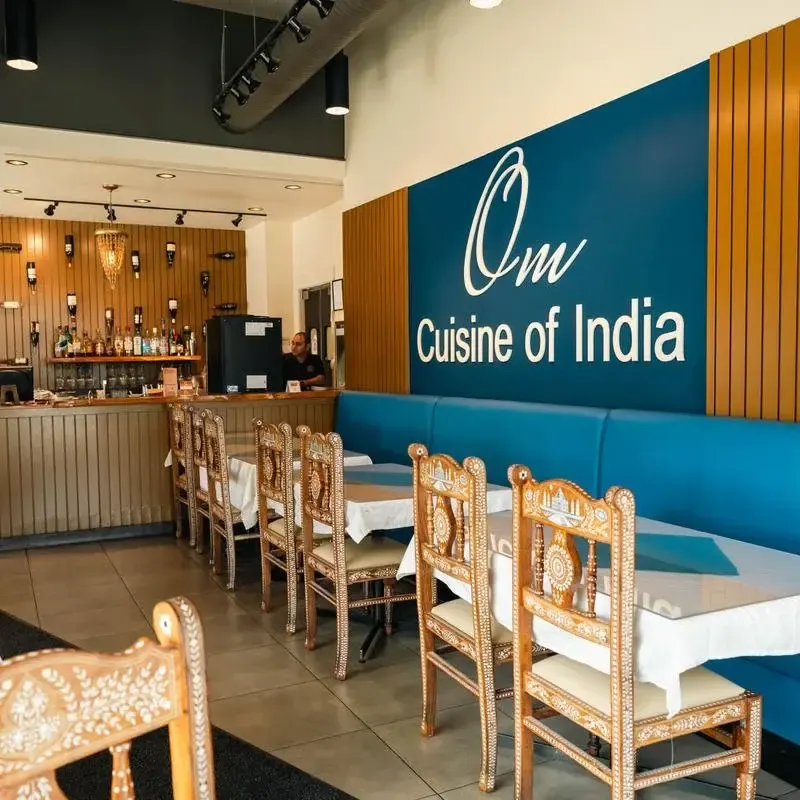 Inside Om Cuisine of India in Haysboro, Calgary — bar, blue banquette, and carved chairs