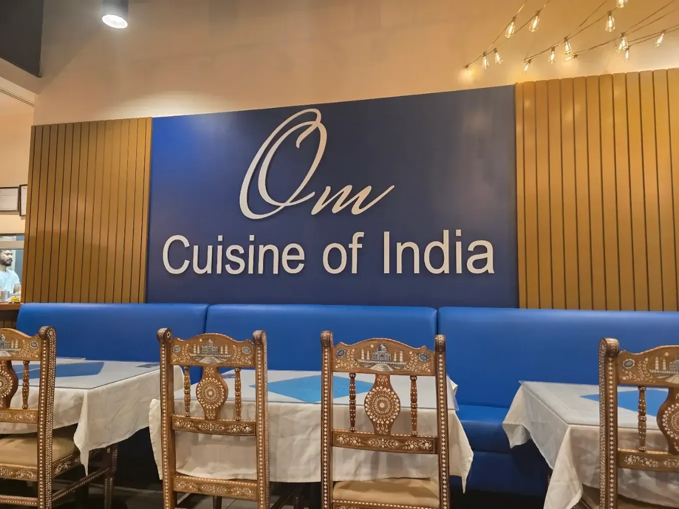 Om Cuisine of India dining room with the restaurant sign and carved wooden chairs
